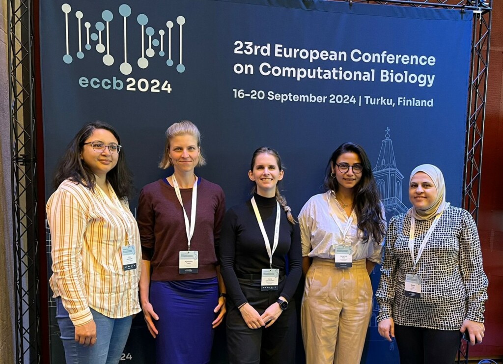 Five people standing in front of a large pop-up banner that reads '23rd European Conference on Computational Biology. 16-20 September 2024. Turku, Finland'